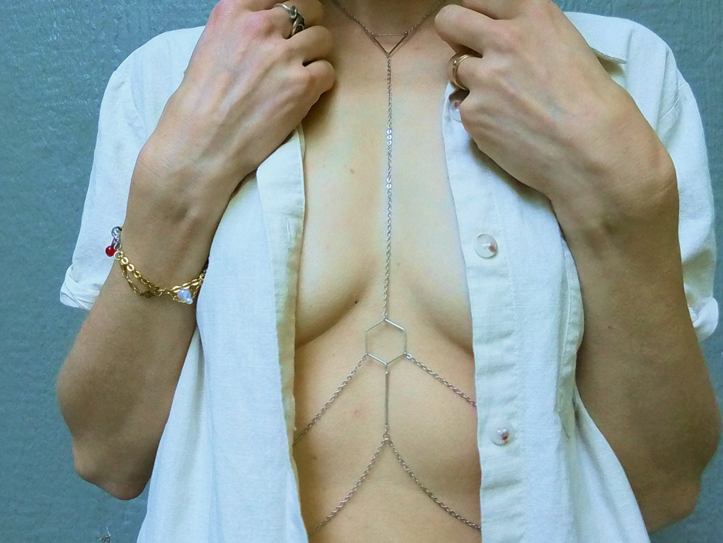 Person wearing a silver hexagonal body chain under a white shirt.