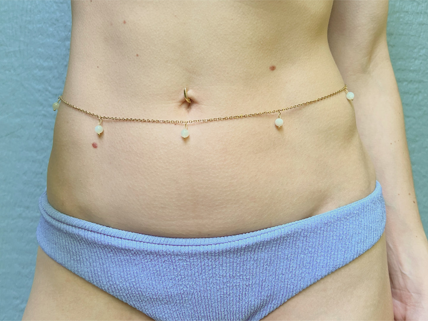 Person wearing a dainty gold belly chain adorned with white moonstone dangles