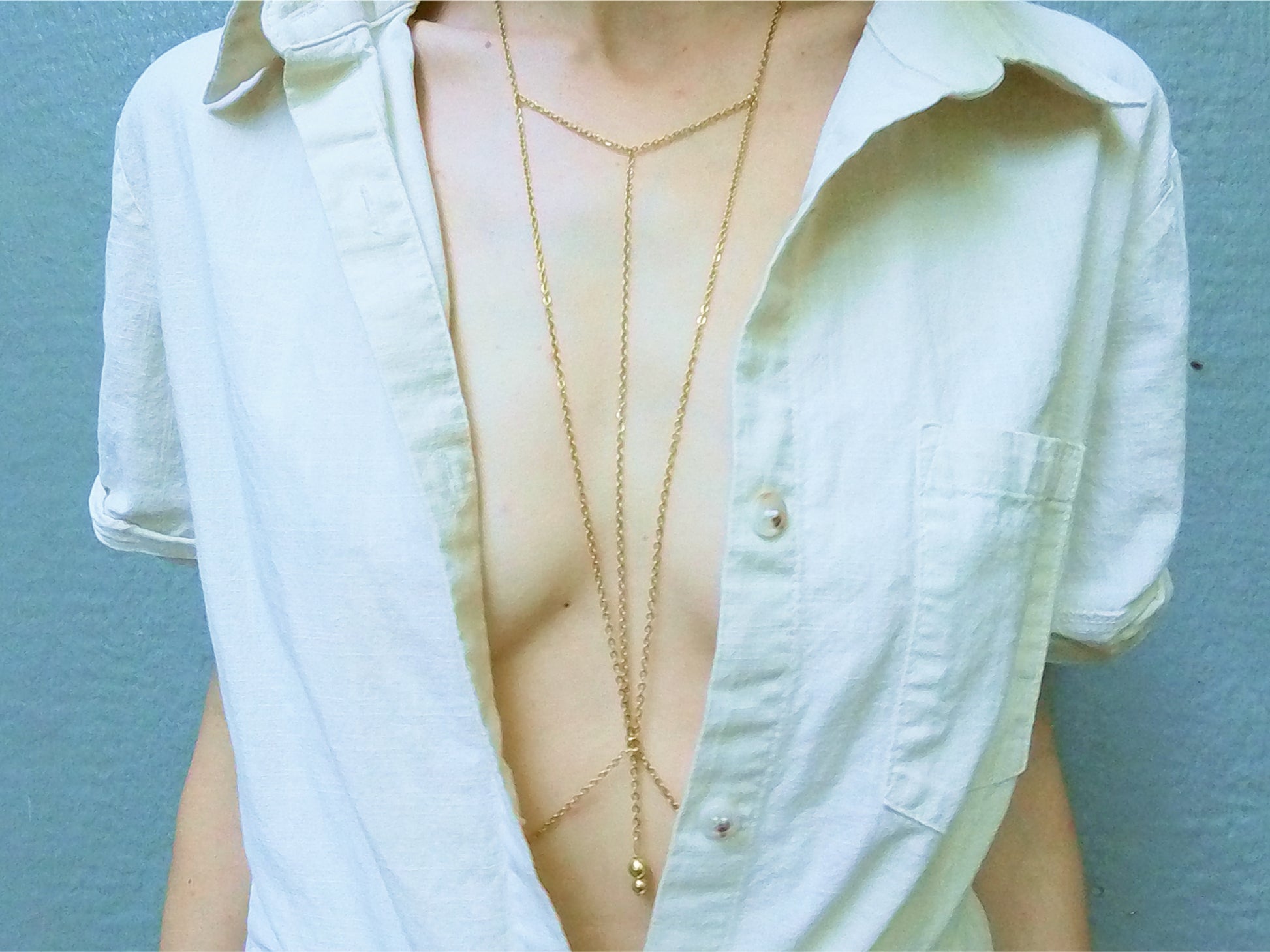 Person wearing a triangular dainty gold body chain under a white shirt