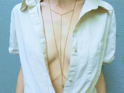 Person wearing a triangular dainty gold body chain under a white shirt