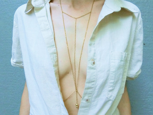Person wearing a triangular dainty gold body chain under a white shirt