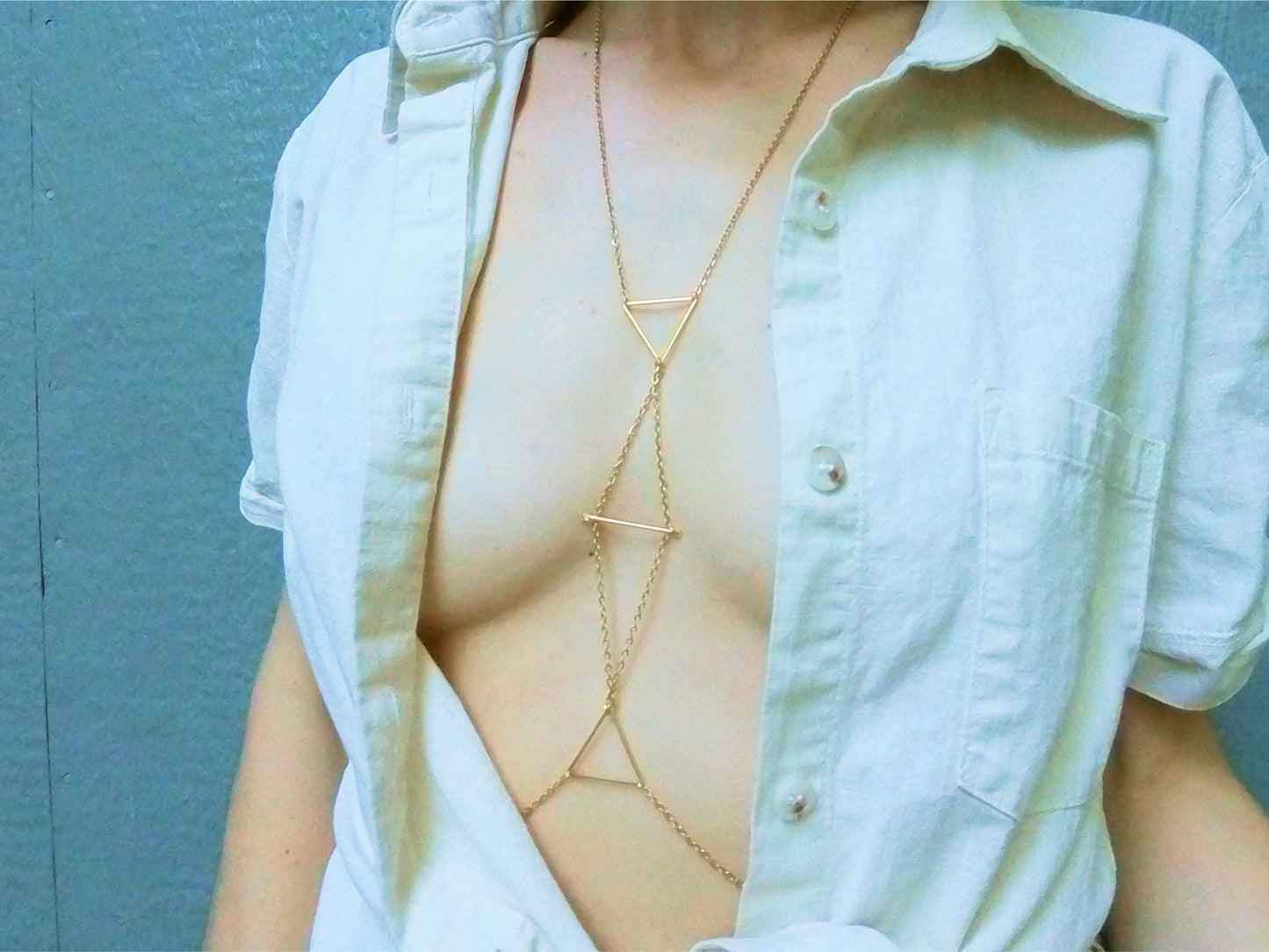 Person wearing a gold intricate body chain with triangle pattern under a white shirt