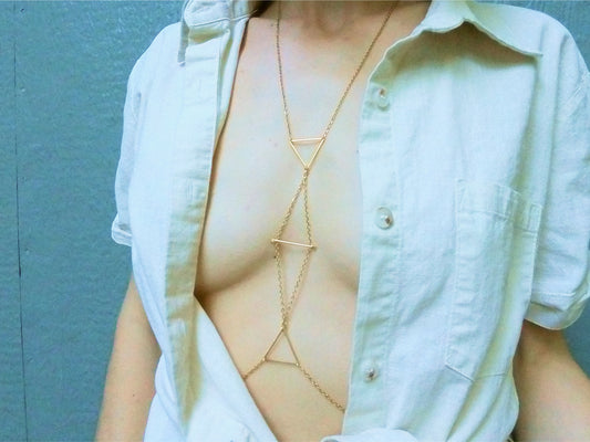 Person wearing a gold intricate body chain with triangle pattern under a white shirt