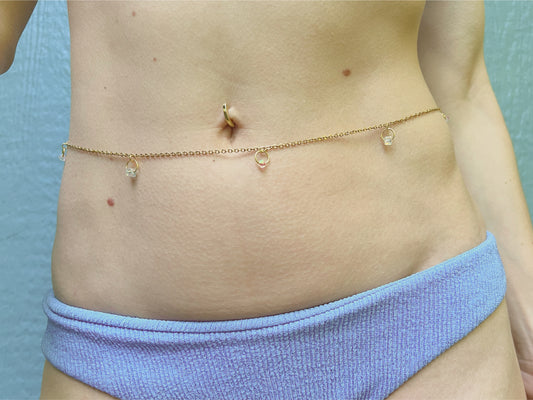 Person wearing a golden belly chain with little rings and crystal beads