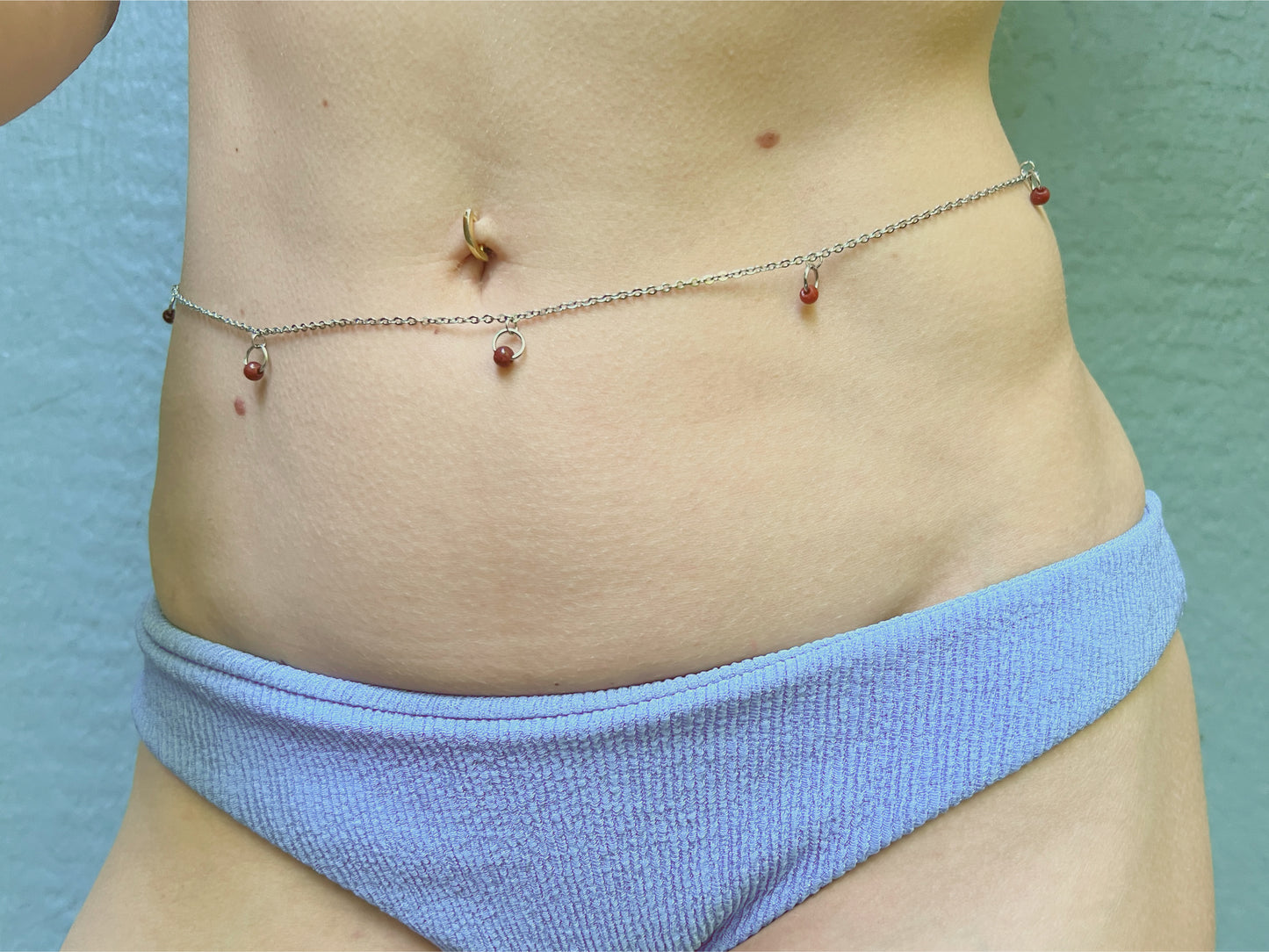 Person wearing a silver waist chain with little o rings and red stones