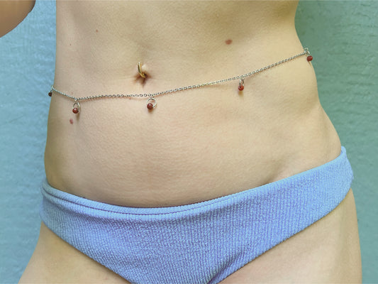 Person wearing a silver waist chain with little o rings and red stones