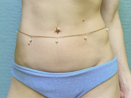 Person wearing a dainty gold belly chain adorned with white moonstone dangles