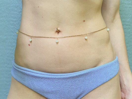 Person wearing a dainty gold belly chain adorned with white moonstone dangles