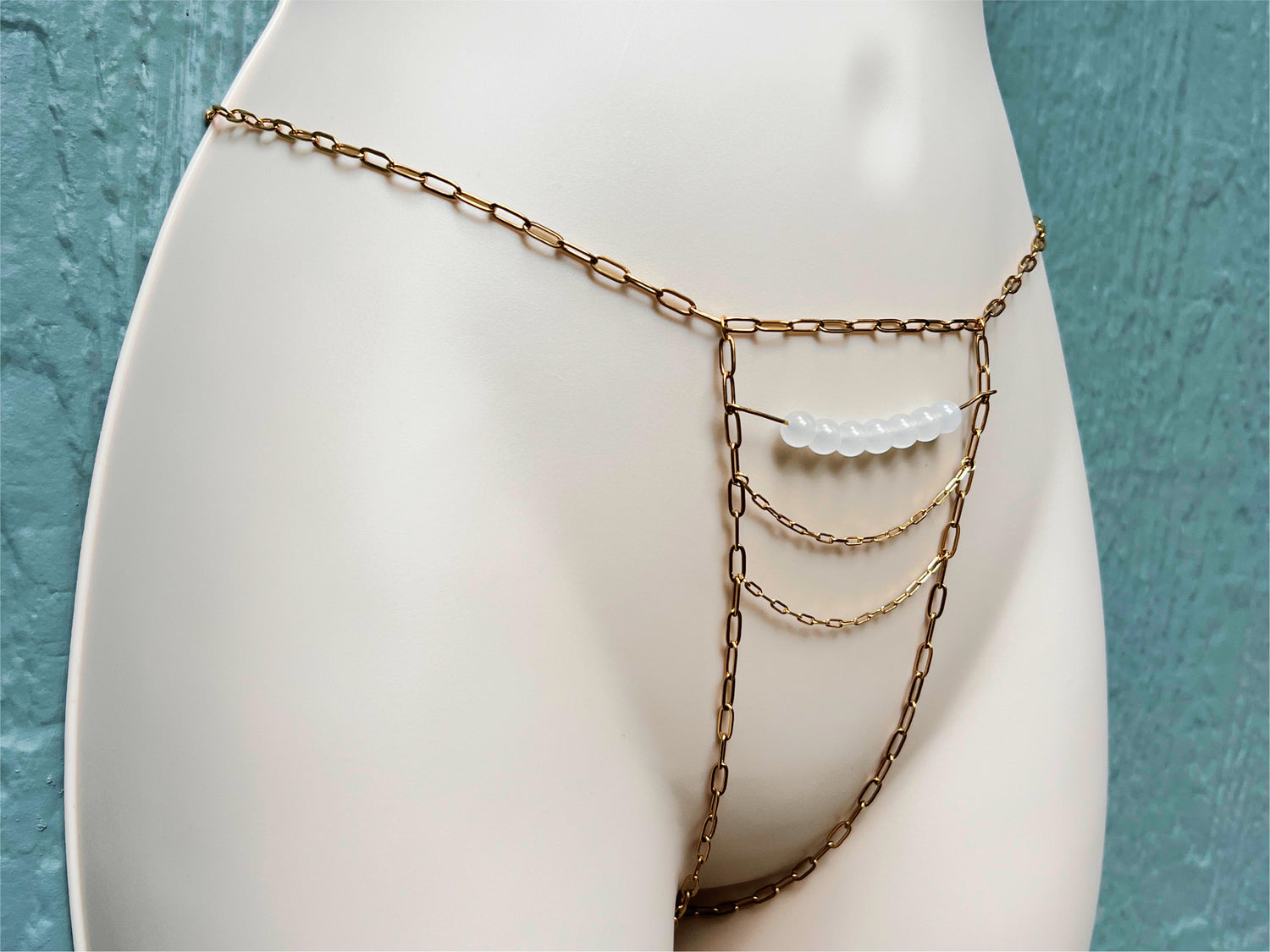 Crotchless panties made of golden chains on a mannequin - thick paperclip chains, with wire and glass beads